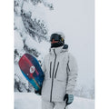 Light grey Burton AK Lz Gore-Tex 2L Down Snowboard Jacket with black zippers and hood worn in a snowy mountain setting.