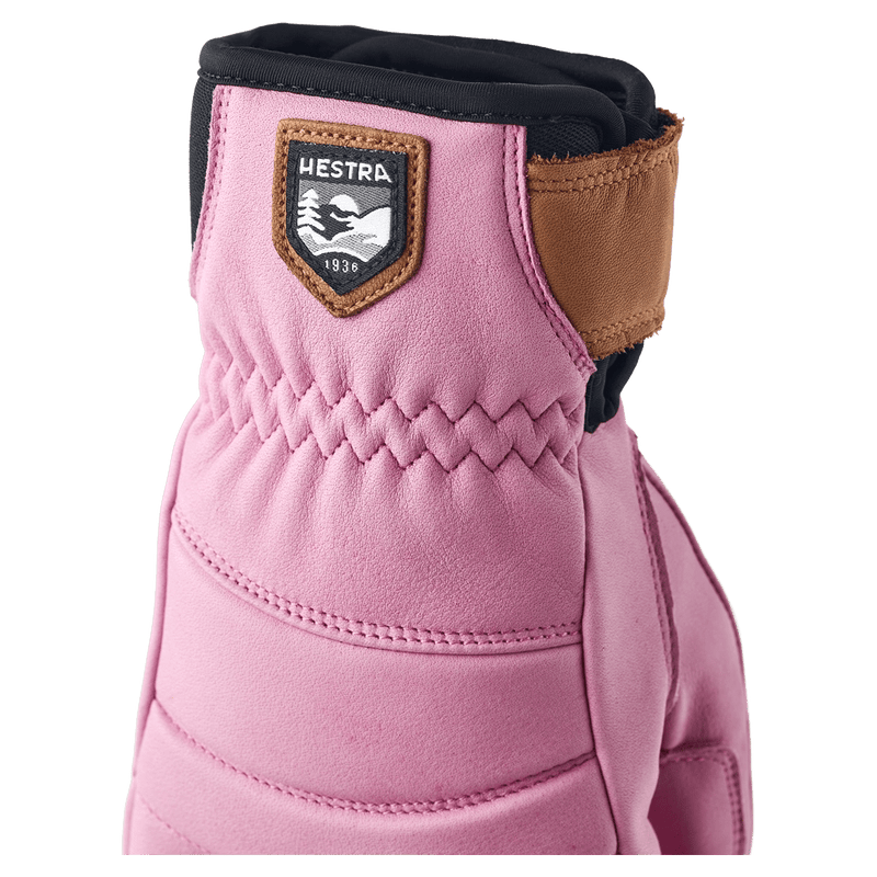 Close-up of a Cerise leather Hestra glove with a brown logo patch, elasticized wrist, and brown leather strap.