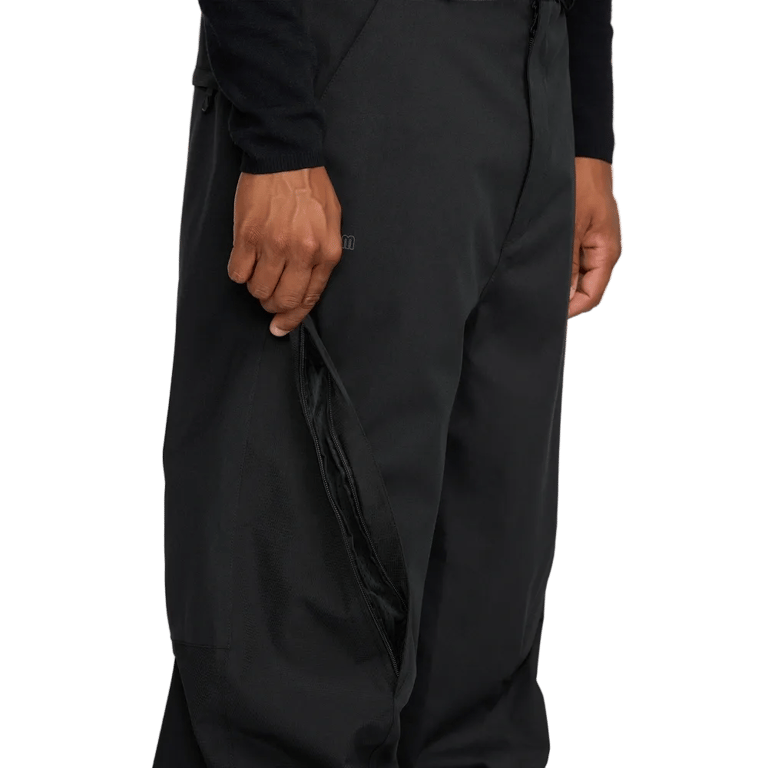 Black Volcom Kleveland snowboard pants with a hand opening a zippered outer thigh vent.