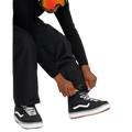 Black Volcom Kleveland snowboard pants with elastic cuffs being adjusted over black and white high-top boots.