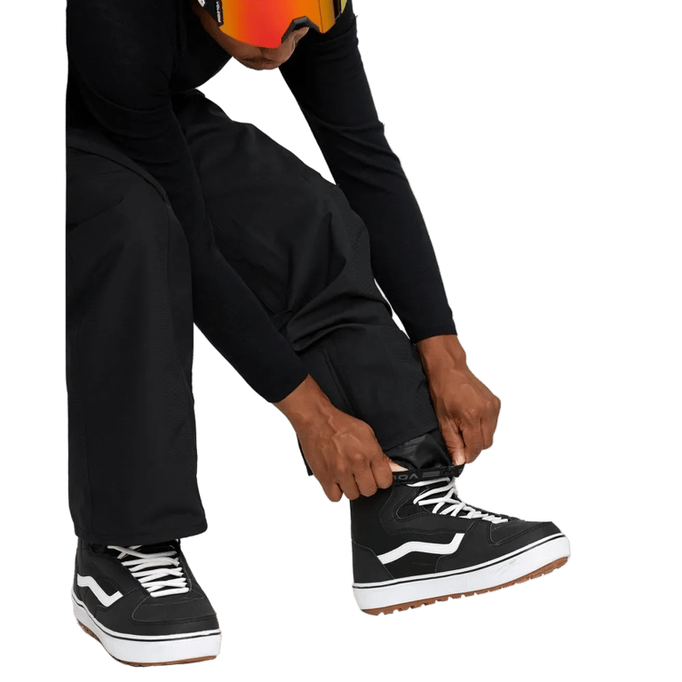 Black Volcom Kleveland snowboard pants with elastic cuffs being adjusted over black and white high-top boots.