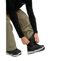 Olive green Volcom Kleveland snowboard pants with adjustable inner gaiter being pulled over black snowboard boots.