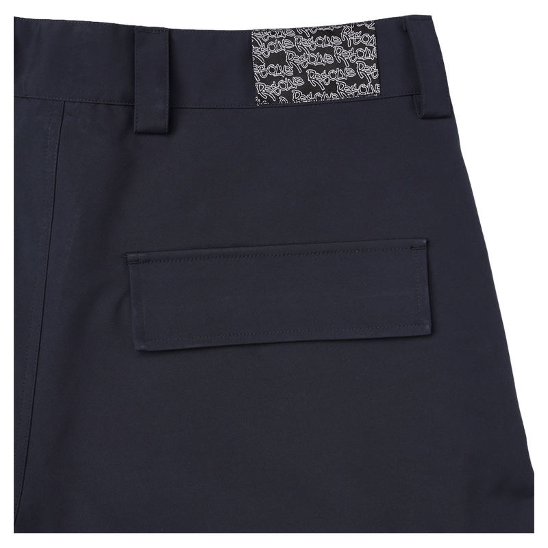 Close-up of navy Resolve Sprinter baggy cargo ski pants showing the waistband, logo patch, and flap back pocket.