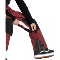 Detail, on-body image of the Rain Gore-Tex Bib Snowboard Pants from Volcom in Burnt Red. Featuring inner thigh vent with zip closure.