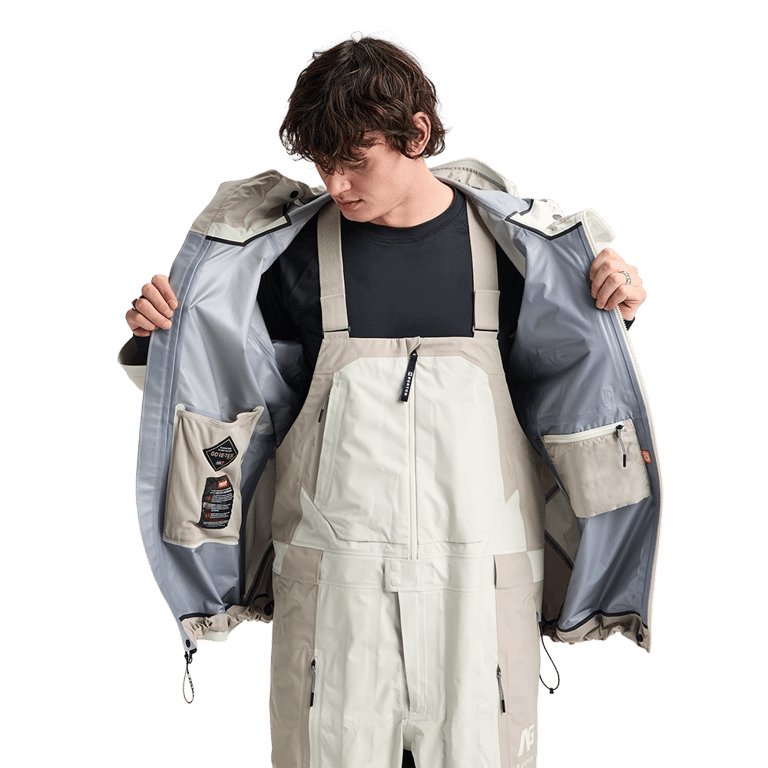 Open beige Analog Hardpack 3L Snowboard Jacket showing grey interior lining and internal pockets over matching bibs.