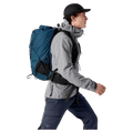Side profile of a blue Arcteryx Aerios 35 backpack with mesh pockets and waist strap worn by a man walking.