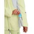 Pale yellow women's Burton Reserve 3-In-1 Snowboard Jacket with a blue lift ticket being placed in a sleeve pocket.
