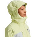 Woman wearing a pale yellow and white Burton Reserve 3-In-1 Snowboard Jacket with the hood up and high collar.