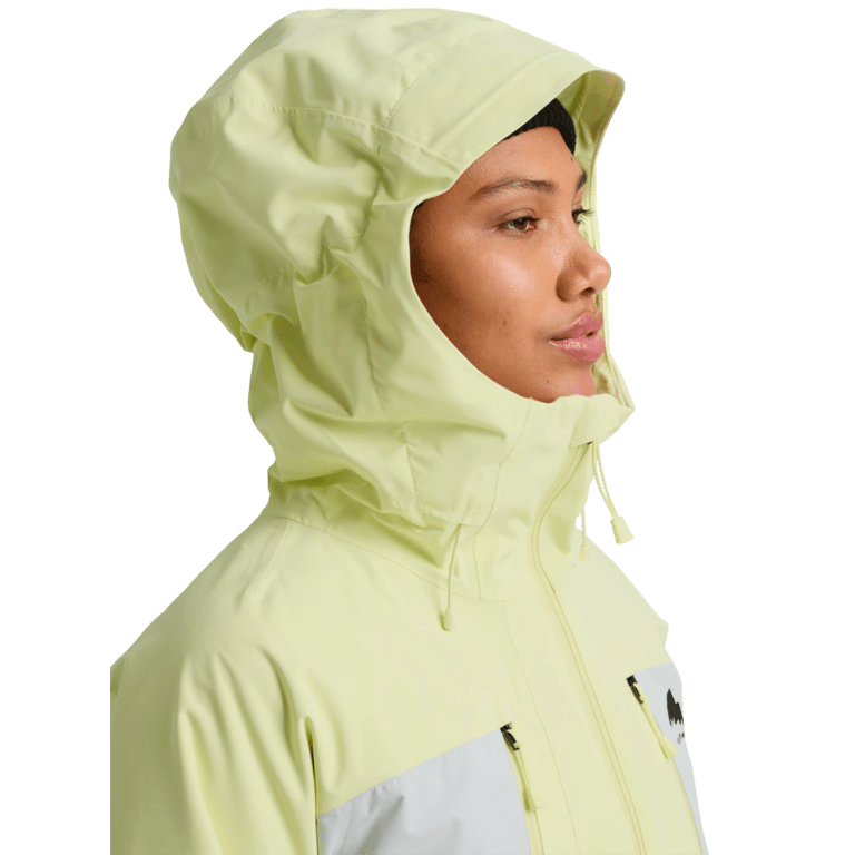 Woman wearing a pale yellow and white Burton Reserve 3-In-1 Snowboard Jacket with the hood up and high collar.