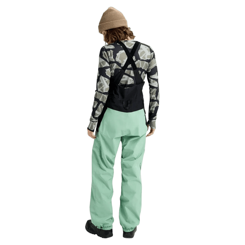 Rear view of women's mint green Burton Reserve Bib Snowboard Pants with black suspenders and a high back panel.