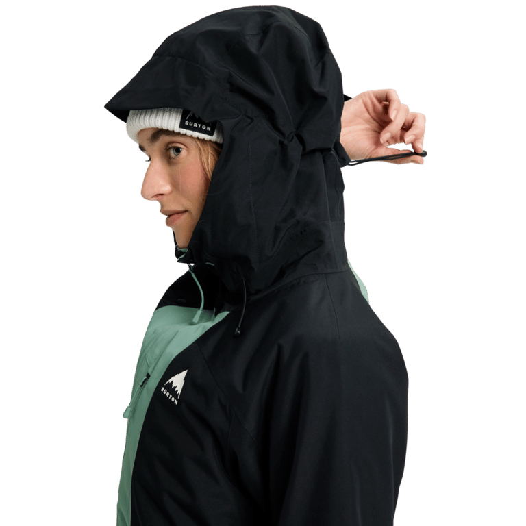 Woman wearing a black and sage green Burton Reserve Insulated Snowboard Jacket with the hood up and a white beanie.