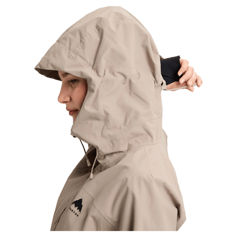 Side profile of a woman wearing a beige Burton Reserve Insulated Snowboard Jacket with the hood up and chest logo.