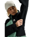 Woman wearing a black and mint green Burton Reserve snowboard jacket showing the underarm ventilation zipper.
