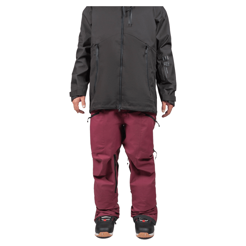 Maroon Endeavor 3L Shelter Bib Snowboard Pants with zippered pockets, worn with a black jacket and snowboard boots.