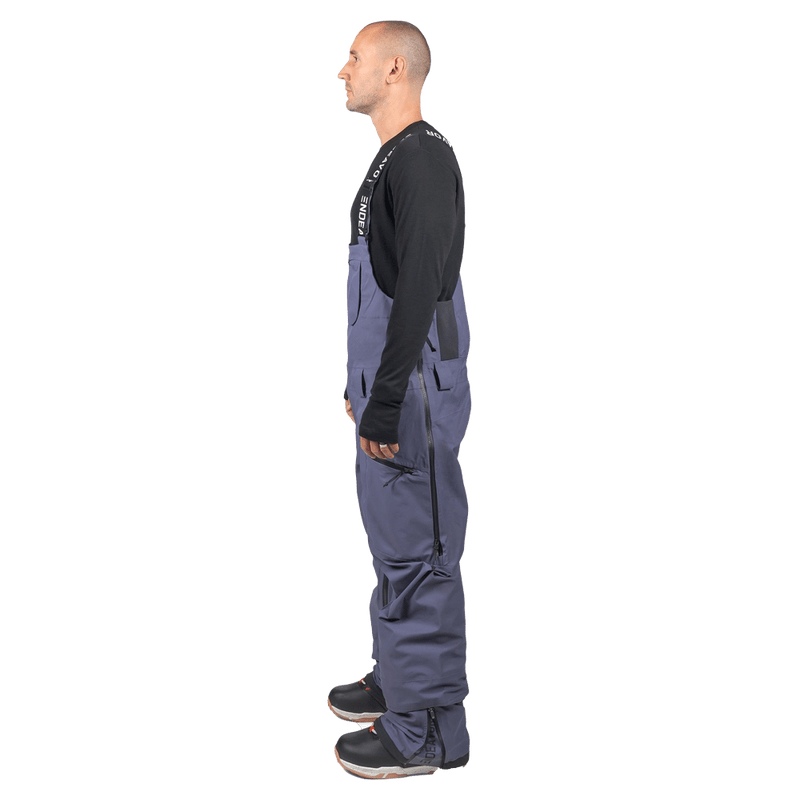 Side profile of slate blue Endeavor 3L Shelter Bib Snowboard Pants with black suspenders and side leg zippers.
