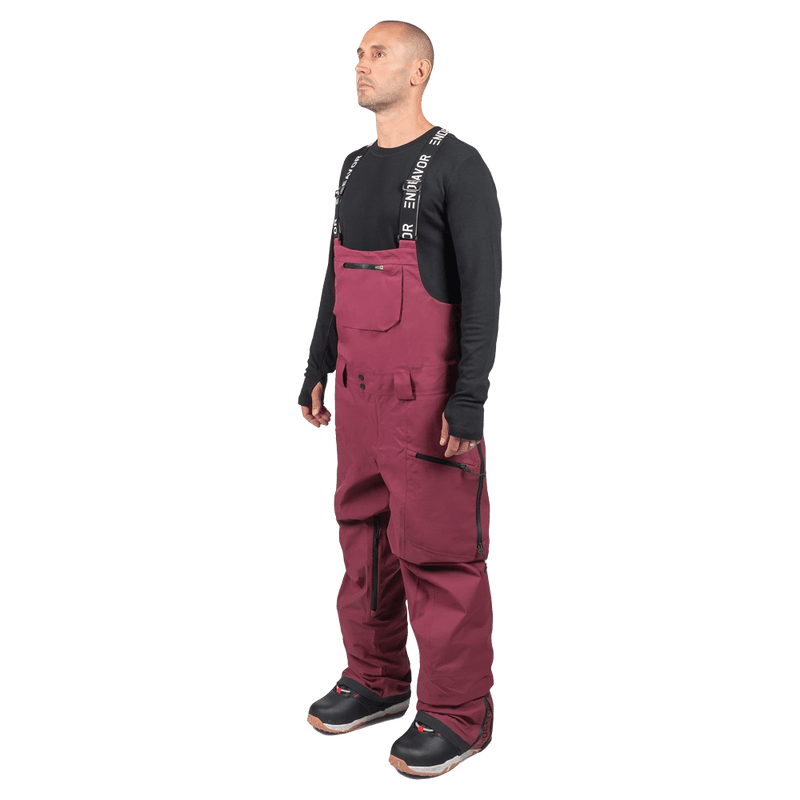 Maroon Endeavor 3L Shelter Bib Snowboard Pants with black branded suspenders and zippered pockets on a model.