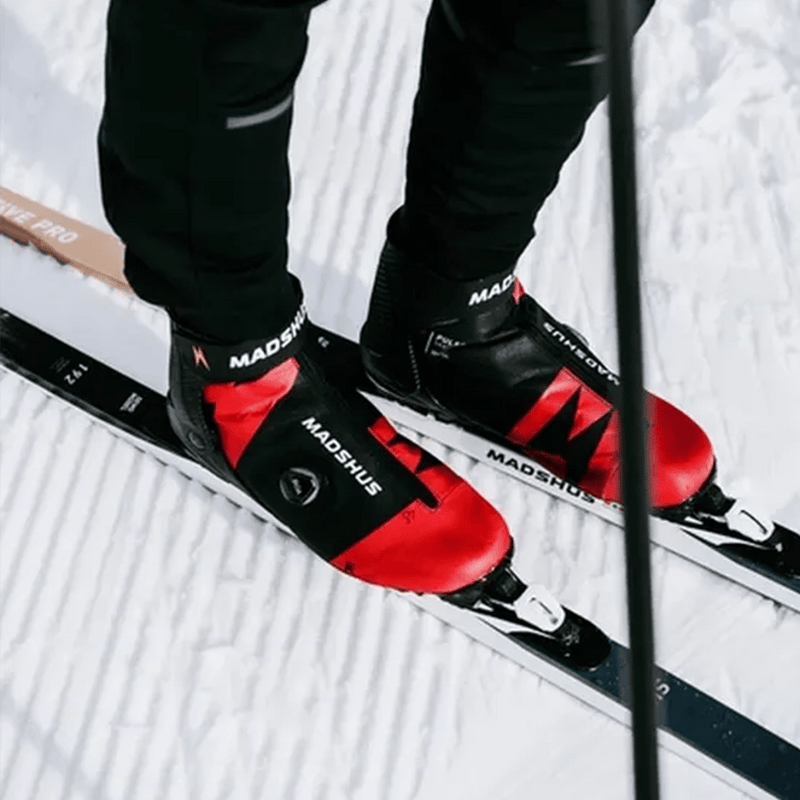 Madshus Pulse Boa Skate Boots in red and black with a side Boa dial, shown on cross-country skis in the snow.