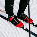 Madshus Pulse Boa Skate Boots in red and black with a side Boa dial, shown on cross-country skis in the snow.