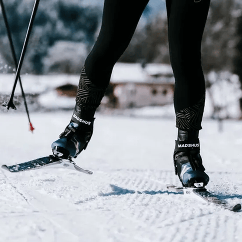 Black and blue Madshus Pulse Boa Skate Boots with ankle straps worn by a skier on a groomed cross-country trail.