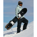 side view of Man standing on snow slope holding Jones 2027 Stratos Snowboard
