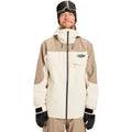Man wearing a cream and tan Quiksilver Radicalo Snowboard Jacket with a hood, chest logo, and black center zipper.