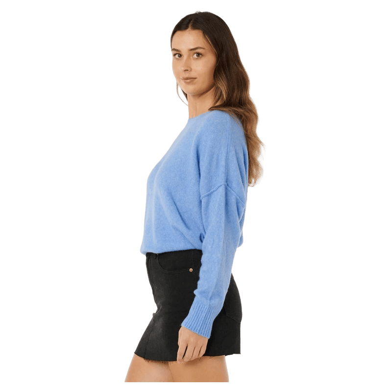 Side profile of a woman wearing a light blue Rip Curl Emily knit sweater with long sleeves and ribbed cuffs.