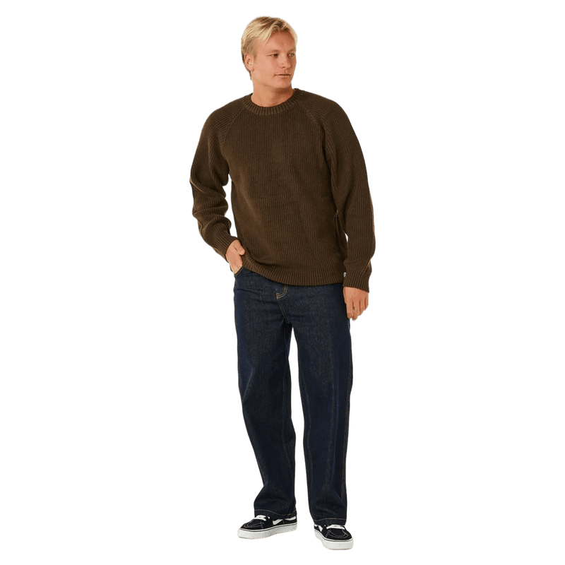 Rip Curl Premium Surf Knit Crew in dark brown, a textured knit jumper with a ribbed crew neck, worn with blue jeans.