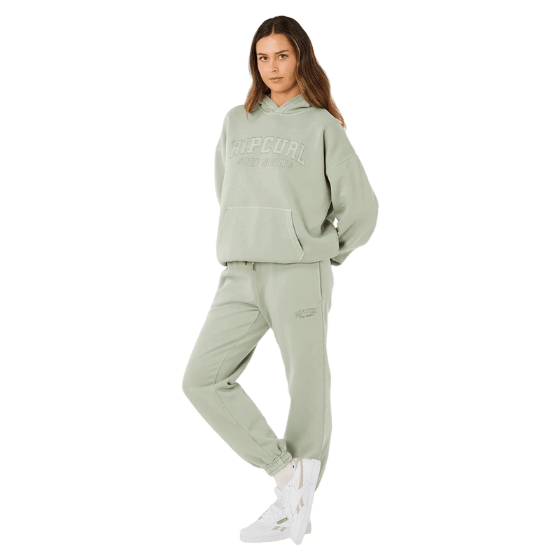 Woman wearing light green Rip Curl Varsity Sports track pants and matching hoodie with white sneakers.