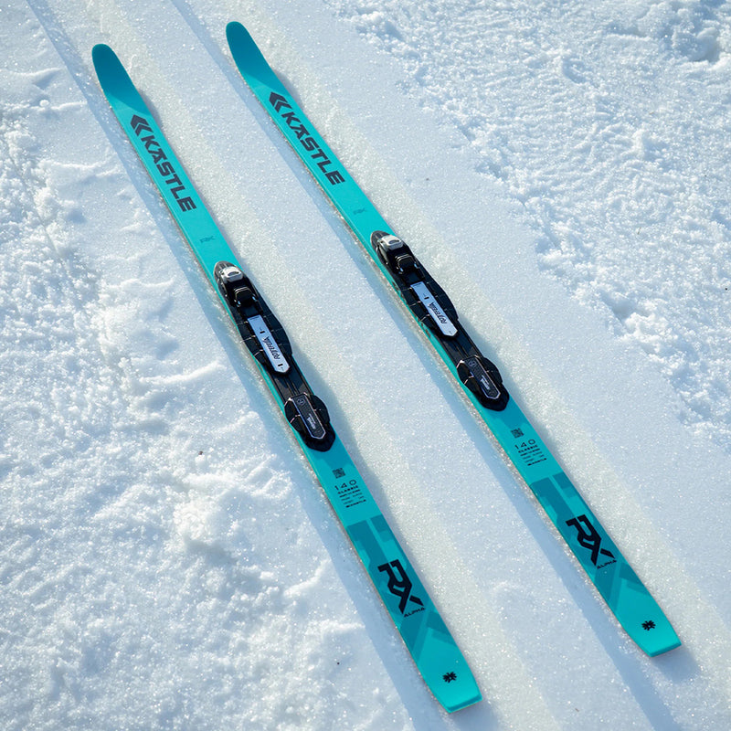 Turquoise Kastle RX Alpha Crown cross country touring skis with black bindings on white snow.