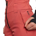 Rojo women's high rise softshell ski pants in burnt orange showing front zipper, side pocket, and logo.