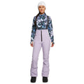 Front view of a woman wearing lavender Rojo softshell high rise ski pants with black suspenders and a front zipper.