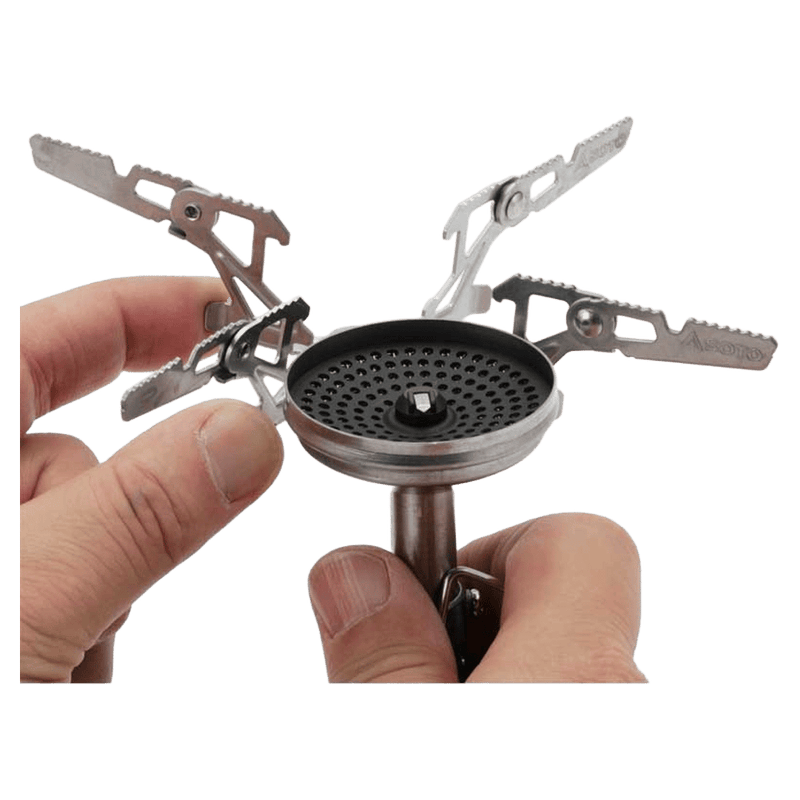 Soto Windmaster camping stove burner head with hands attaching the four-prong stainless steel pot support.