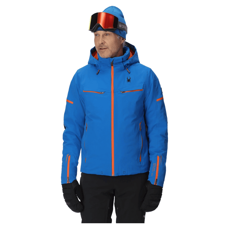 Blue Spyder Monterosa ski jacket with orange zipper accents and hood, worn by a man in ski gear.