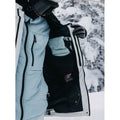 Interior of a white and blue Burton AK snowboard jacket showing a black mesh pocket and quilted down lining.