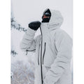 Light grey Burton AK Lz Gore-Tex down snowboard jacket with hood and black zippers worn in a snowy outdoor setting.