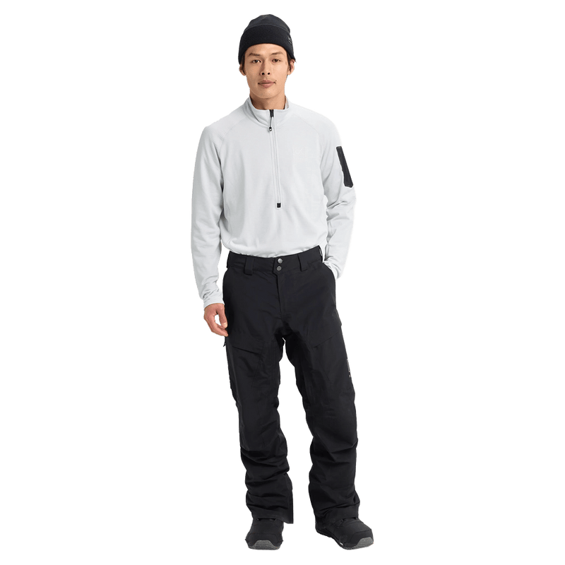 Front full body view of a man wearing the Burton AK Swash Gore-Tex 2L Snowboard Pants in Black with a white fleece top and black beanie