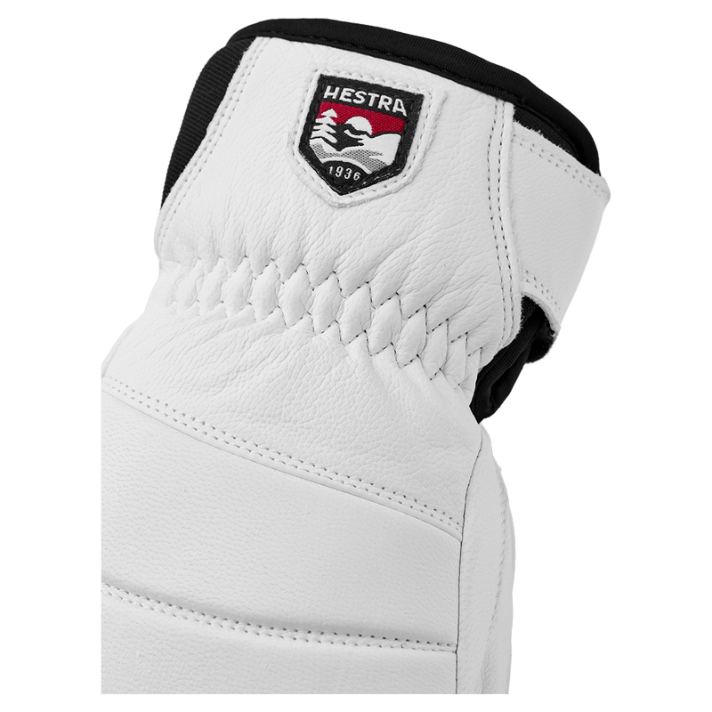 White leather Hestra glove featuring a logo patch, elasticated wrist, and black cuff detail.