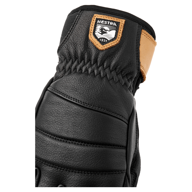 Close-up of a black Hestra Leather Fall Line glove featuring quilted leather padding, elastic wrist, and tan logo patch in colour Black