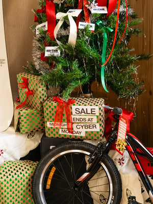 Christmas tree with wrapped gifts and a bicycle underneath, against a brown wall.