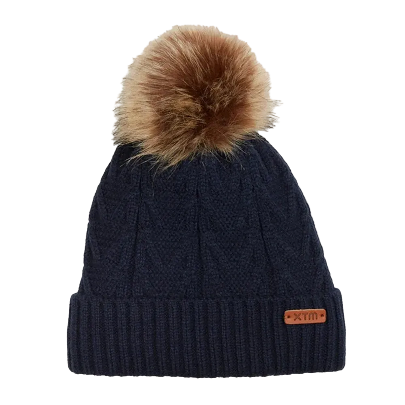 View of the Isla Beanie in Navy. Featuriing a cable knit design with ribbed fold up hem, leather brand tag and brown fur pom pom. 