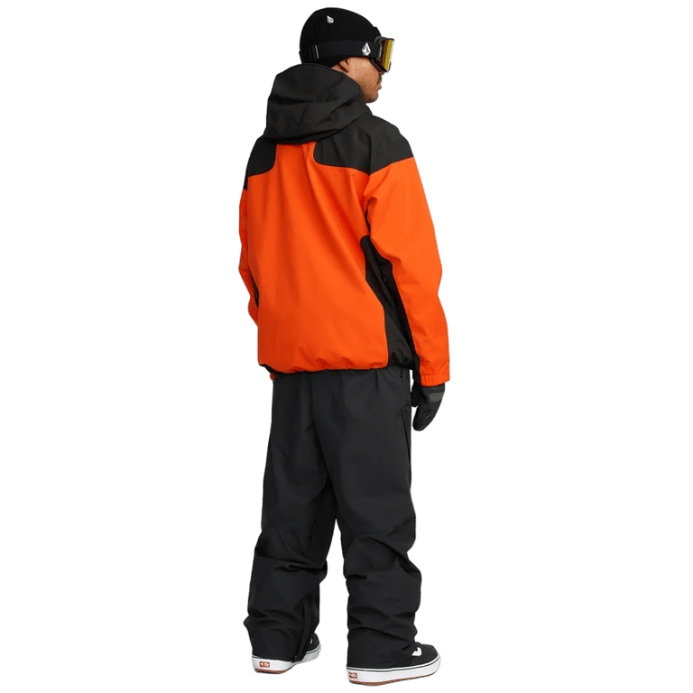 Rear view of Volcom Kleveland black snowboard pants paired with an orange and black jacket.