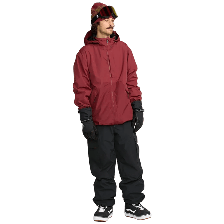 Man wearing black Volcom Longo Gore-Tex snowboard pants with cargo pockets, a red jacket, and black gloves.