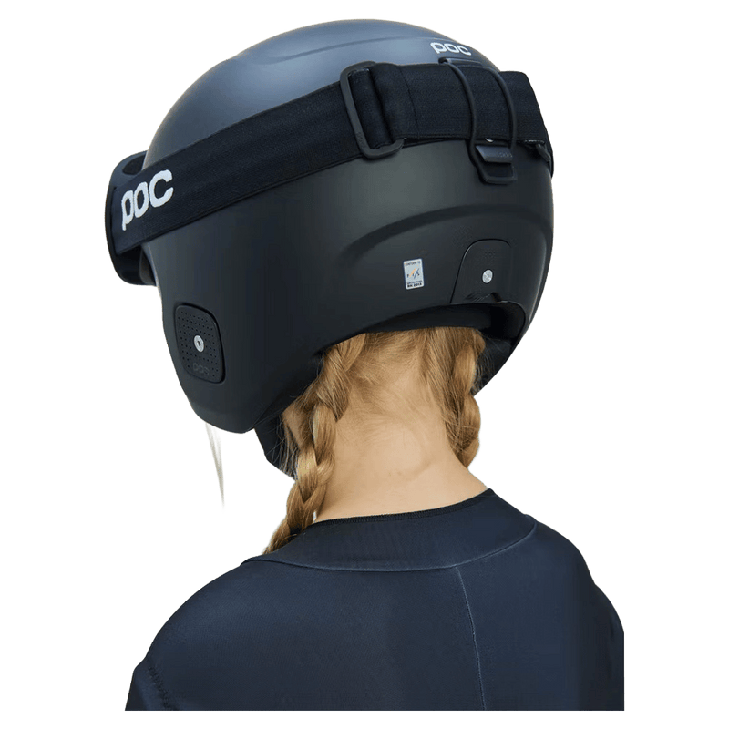 Rear view of a child with blonde braids wearing a matte black Poc Skull Dura Jr kids' ski helmet with black goggles.