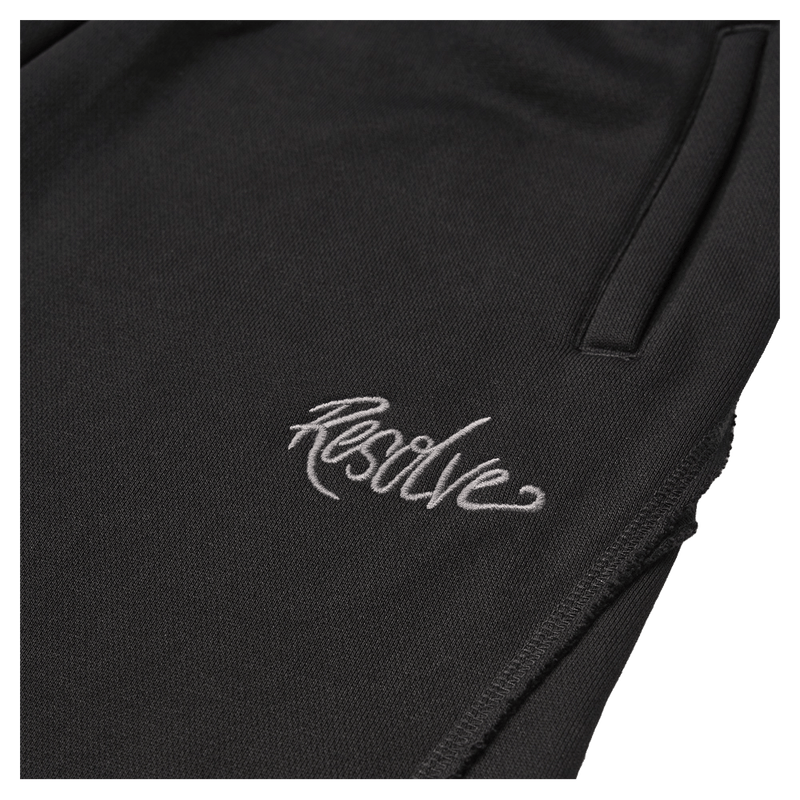 Close-up of black Resolve Daily Sweatpants with white embroidered script logo and side pocket.