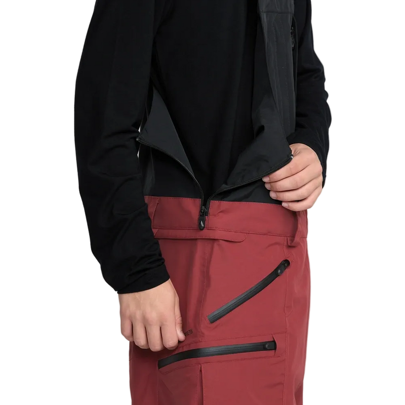 Detail, on-body image of the Rain Gore-Tex Bib Snowboard Pants from Volcom in Burnt Red. Featuring Neoprene Jersey at Side Waists with zip fastening.