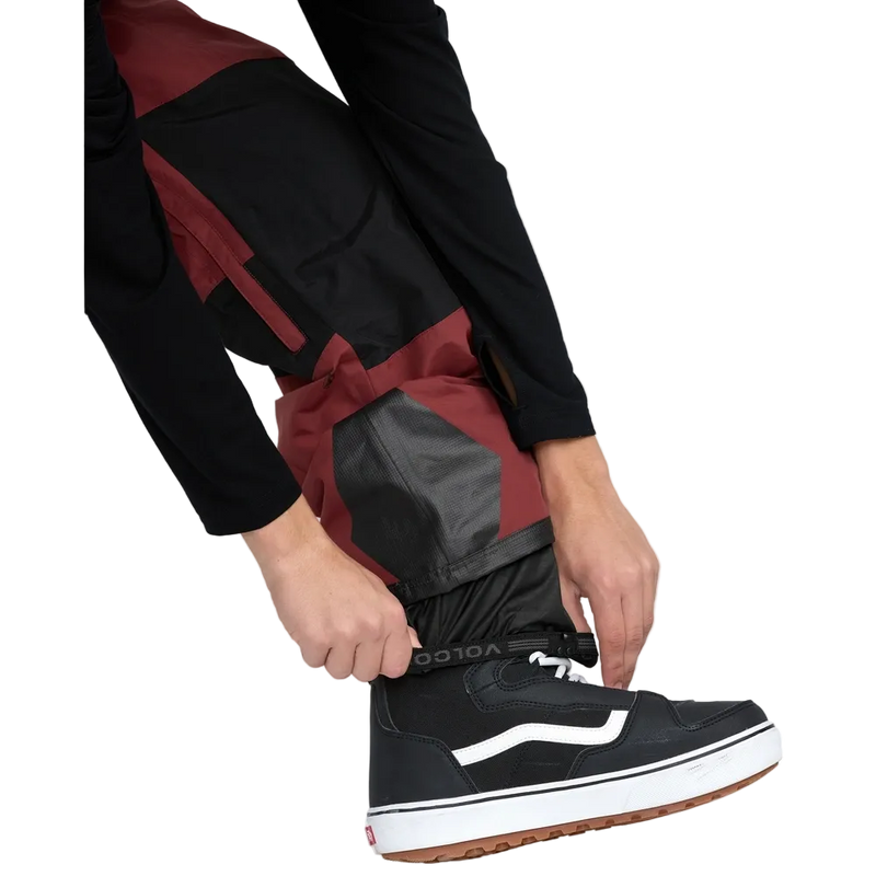 Detail, on-body image of the Rain Gore-Tex Bib Snowboard Pants from Volcom in Burnt Red. Features elasticated storm cuffs.