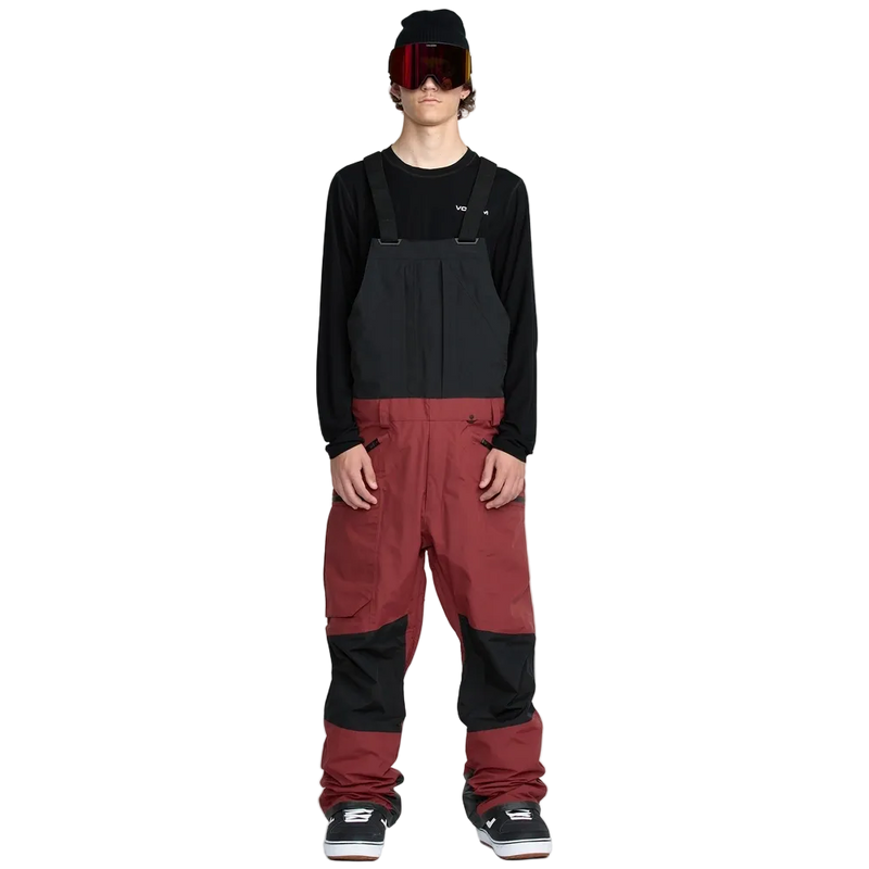 Front, on-body image of the Rain Gore-Tex Bib Snowboard Pants from Volcom in Burnt Red. Featuring adjustable shoulder straps, belt loops, ticket loop, side pockets with zip closure, and side cargo style pockets with zip closure. Contrast Black colour through upper bib and knee patches.