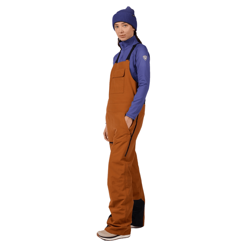 Side view of the Rossignol Outerlimits Insulated Bib in DEEP CARAMEL colourway, women model