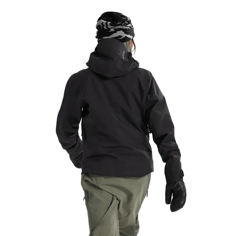 Rear view of a woman wearing the Sentinel Ski Jacket in Black featuring a helmet compatible hood. 