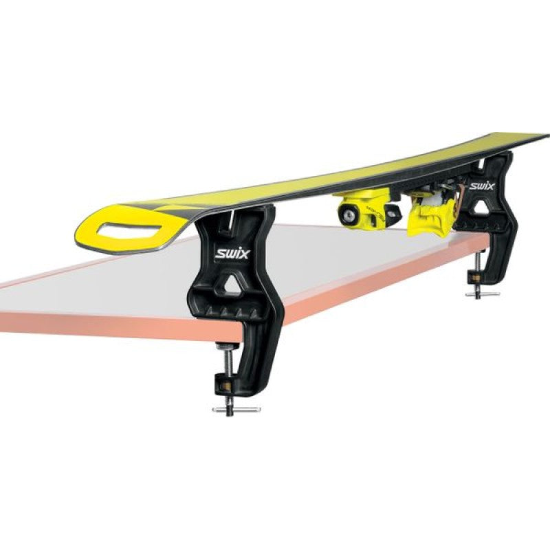 A pair of Swix Tuning vise in black ballistic plastic with silver metal screws vises on a table with a single ski laying on top